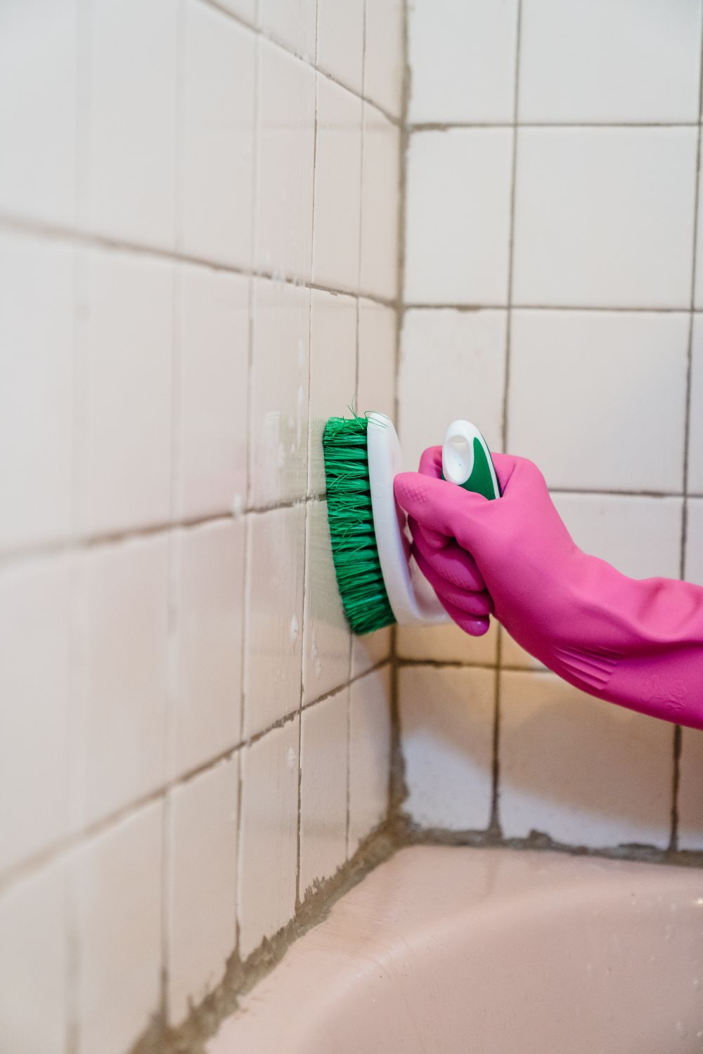 Gloved hand scrubbing tile grout in a bathroom